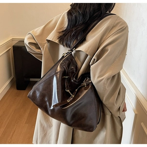 Detail of dark brown large tote bag with polished finish and gold buckle on shoulder