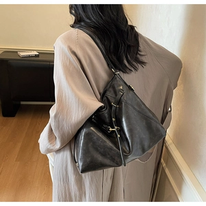 Minimalist black oil wax leather tote bag shown on a model in a stylish trench coat