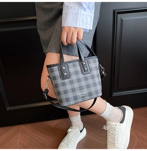 Detail of checkered tote bag with leather handles and silver metal rivet accents