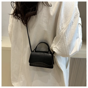 Detail of a black faux crocodile mini handbag with a curved flap and silver hardware