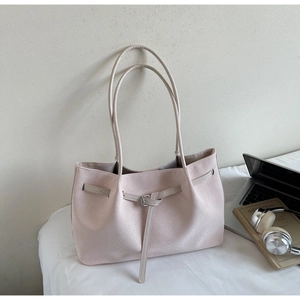 Detail of light beige woven tote bag with buckled straps on a desk with a laptop