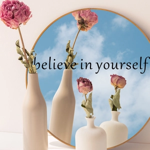 Detail of matte beige ceramic vase with dried flowers and 'believe in yourself' quote