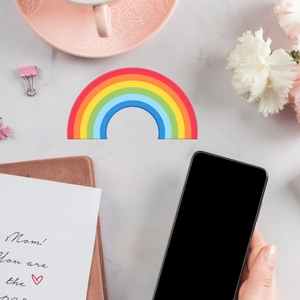 Glow-in-the-dark mini rainbow wall sticker held next to a phone for size comparison