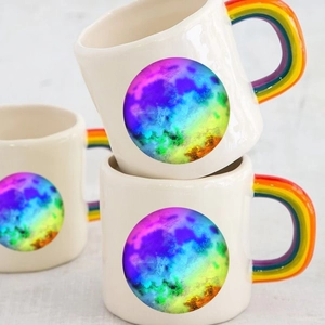 Ceramic mugs with colorful rainbow handles and vibrant planet patterns on a neutral cloth