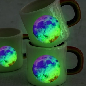 Close-up of luminous celestial patterns on mugs glowing purple and green in the dark