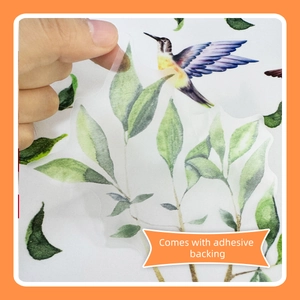 Detail showing hand peeling a transparent hummingbird and leaf sticker with adhesive backing