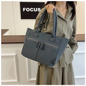 Detail of grey-blue canvas tote bag featuring double front zipper pockets and shoulder straps