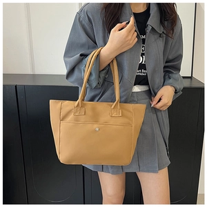 Detail view of khaki nylon tote bag with metal button pocket worn by a model