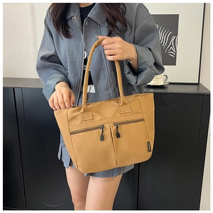 Detail of camel canvas tote bag showing functional zipper pockets and fashion label