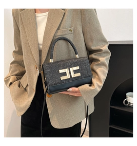Macro detail of the metallic logo buckle and sparkly texture on a black crossbody bag