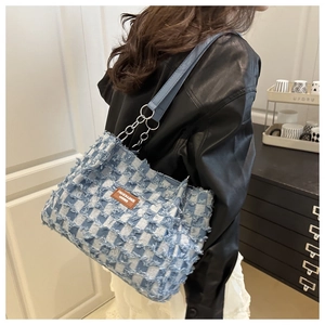 Détail du cabas en denim à carreaux avec étiquette en cuir et bandoulière à la main