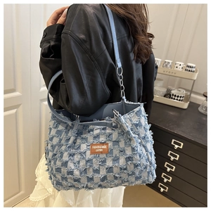 Détail du sac cabas en denim à carreaux bleus avec bords effilochés et étiquette en cuir