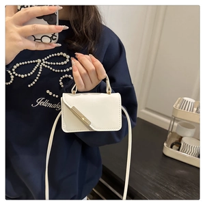 Detail showing white mini square crossbody bag with gold metal trim and delicate strap