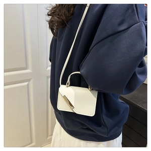 Minimalist white leather crossbody bag with gold buckle on model in modern home setting