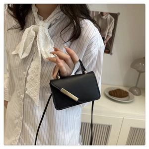 Detail of a black mini crossbody bag with a gold metal bar accent on the flap