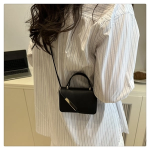 Stylized lifestyle shot of a black mini crossbody bag with a sleek gold diagonal bar detail