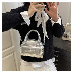 Silberne Schleifenhandtasche mit Spitzenbesatz, getragen von einem Model in Innenräumen