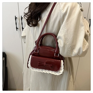 Burgunderrote Lackleder-Bowlingtasche mit Schleife und Spitze zum Trenchcoat getragen