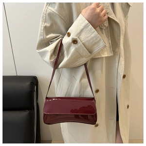 Detail of dark red patent leather shoulder bag with sleek rectangular flap and fine strap