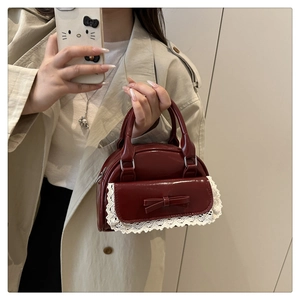 Detail der weinroten Lackledertasche mit Spitzenborte und Vintage-Schleifendekor