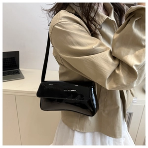 Minimalist black patent leather underarm bag worn over the shoulder in a modern setting