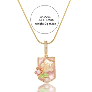 Détail du pendentif doré avec émail rose, perle, motifs floraux et accents de feuilles