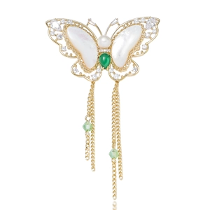 Detail of gold butterfly brooch featuring white mother of pearl and green gemstone fringe