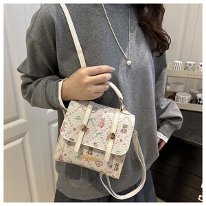 Detail view of white mini square bag with floral prints and golden circular metal handle