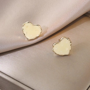 Elegant heart-shaped gold earrings with white enamel on champagne silk background