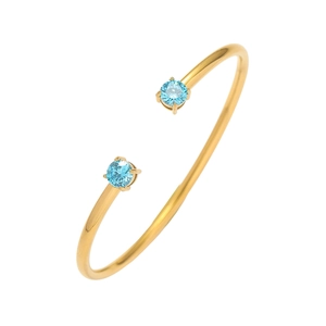 Dettaglio di un bracciale rigido dorato con due pietre rotonde di colore azzurro