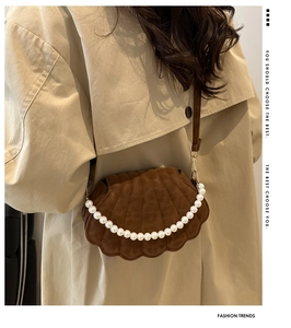 Close-up of brown shell bag with pearl trim on a model wearing a beige trench coat