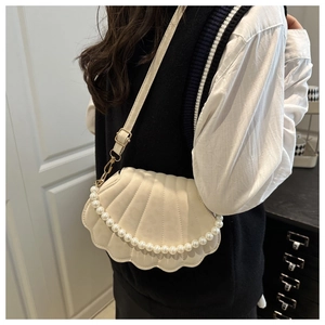 Detail of cream shell-shaped crossbody bag with pearl handle and metal strap