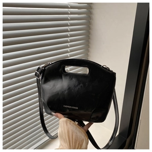 Detail of glossy black handbag with oval cutout handle and silver fashion text printing