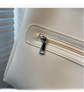Close-up of smooth silver metal zipper and textured cream leather on the shoulder bag