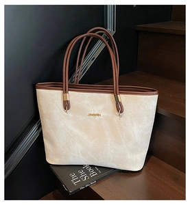 Dettaglio della borsa tote in tessuto beige con finiture in pelle marrone e logo dorato