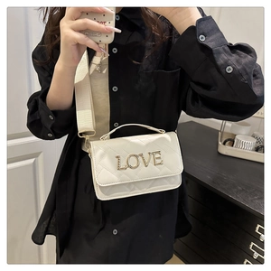 Détail d'un sac bandoulière blanc matelassé avec lettrage LOVE doré et sangle large