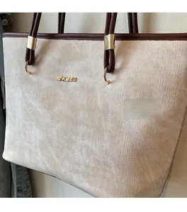 Detail of beige textured tote bag with dark brown trim and golden metal logo hardware