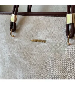 Detailed view of beige tote bag with Jingpin metal logo and dark brown leather handle