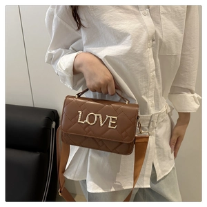 Detail of quilted brown leather bag with gold LOVE lettering and wide fabric strap