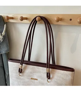 Detail of slim brown shoulder straps and gold logo on off-white textured tote bag