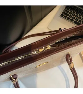 Close-up of golden hardware zipper and logo on a beige woven commuter tote bag