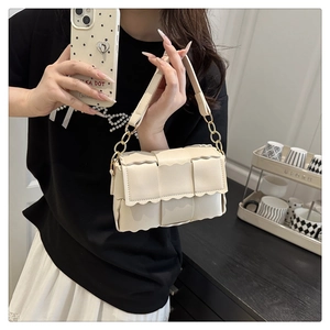 Détail du sac oreiller tressé crème avec bords ondulés uniques et bandoulière chaîne dorée