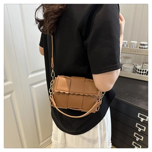 Close-up of brown woven leather crossbody bag with scalloped edges and gold chain detail