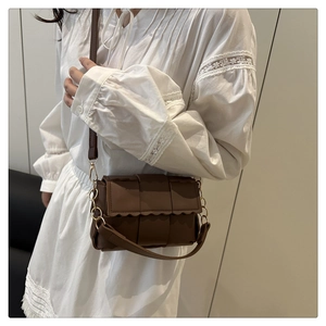 Detail of a brown woven shoulder bag with wavy flap edges and metallic chain strap