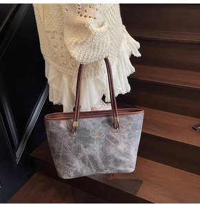 Close-up of retro denim tote bag with brown handles and golden logo on stairs