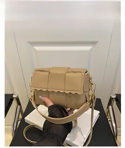 Détail d'un sac bandoulière tissé kaki avec bords festonnés et détails de chaîne dorée