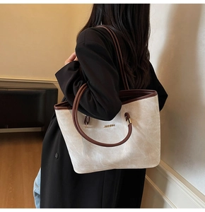 Dettaglio di una grande borsa tote in tela crema con finiture in pelle marrone e logo