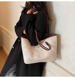 Detailed view of beige tote bag with brown straps worn by model in black coat
