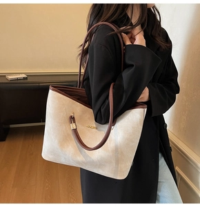 Dettaglio della grande borsa tote in tela beige con manici in pelle marrone sulla spalla
