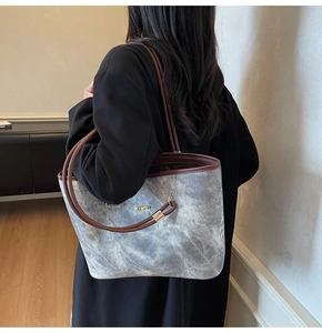 Dettaglio della borsa tote grigia con manici in pelle marrone e placca logo in metallo dorato